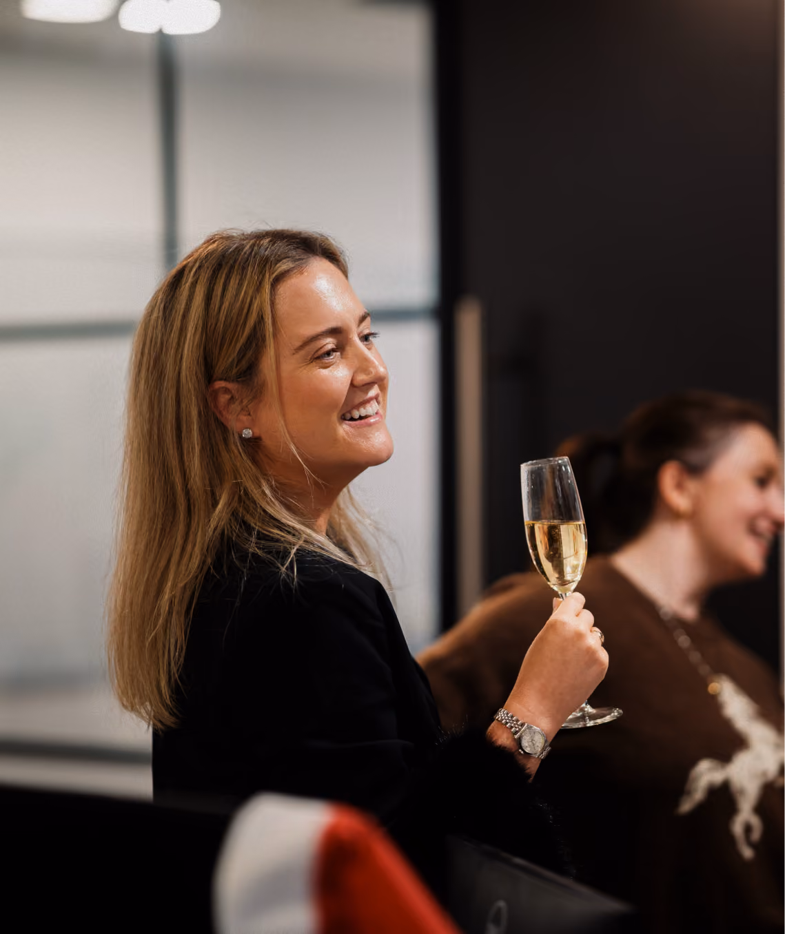 Smiling woman holding a glass of champagne at a social gathering indoors.