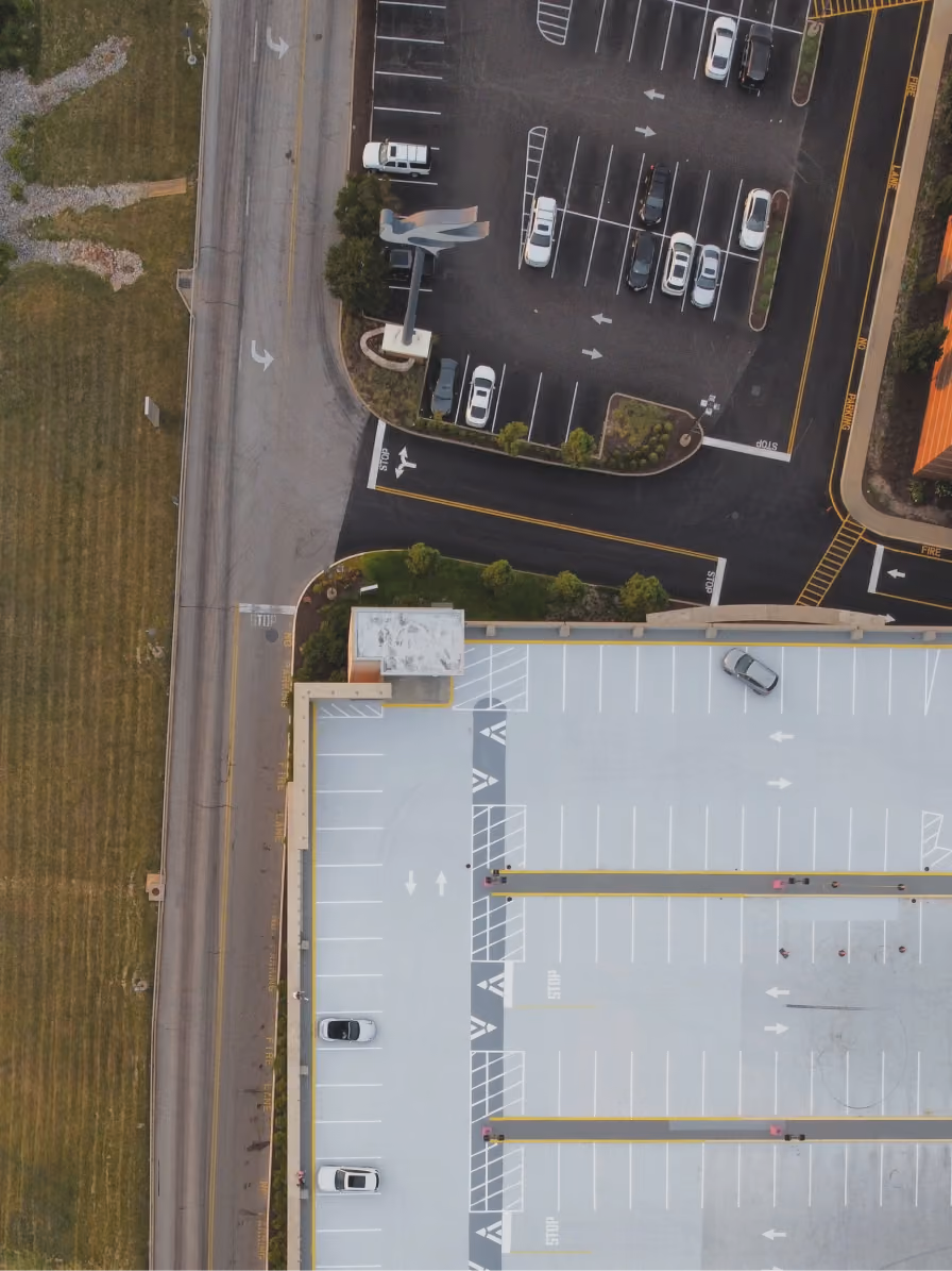Aerial view of a mostly empty multi-level parking lot with cars and adjacent road.
