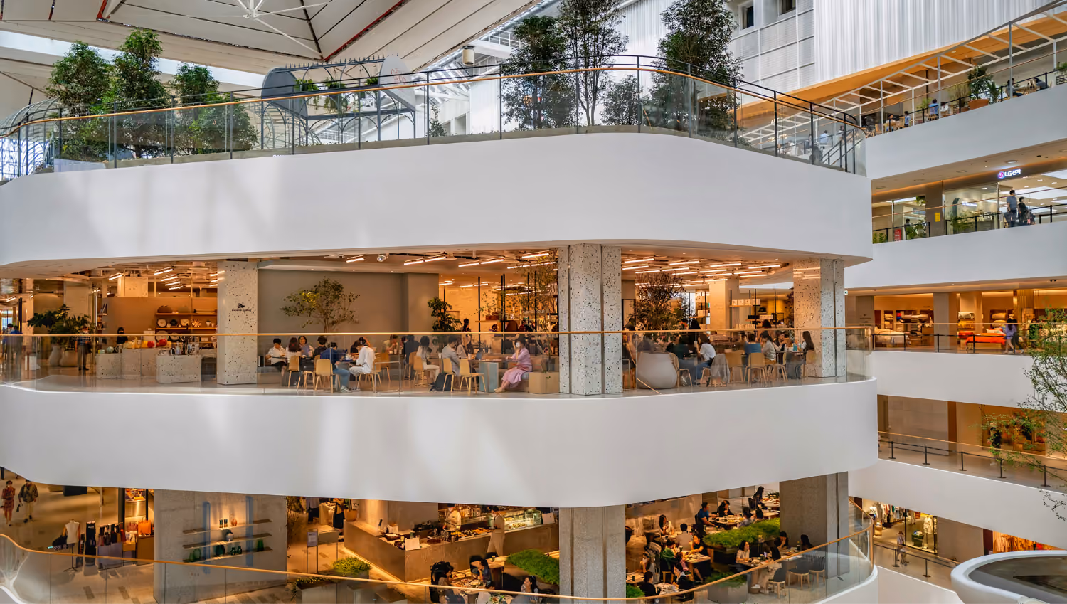 Multi-level indoor shopping mall with people dining on the upper floors under natural light.