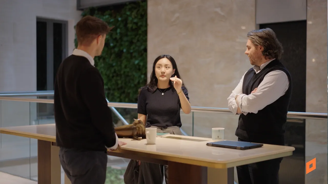 Three people standing around a table in conversation in a modern indoor space.