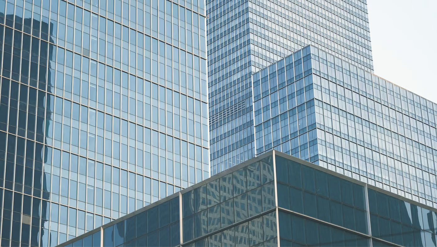 Close-up view of modern glass skyscrapers reflecting light and nearby buildings in a cityscape.