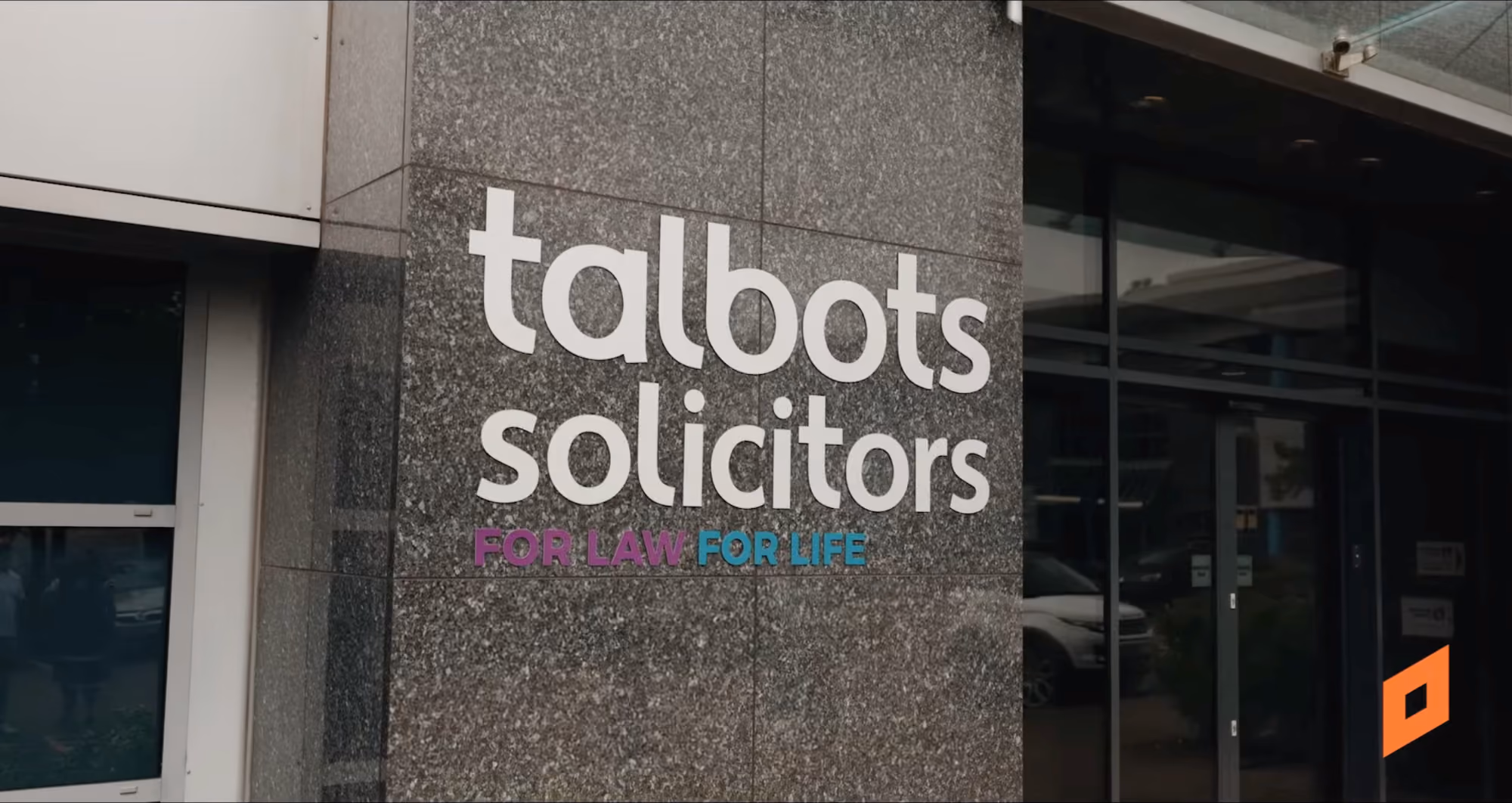 Sign on a building wall reading 'talbots solicitors FOR LAW FOR LIFE' in white, purple, and blue letters.