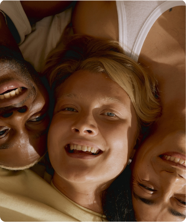 Three friends lying close together smiling, viewed from above with faces touching.