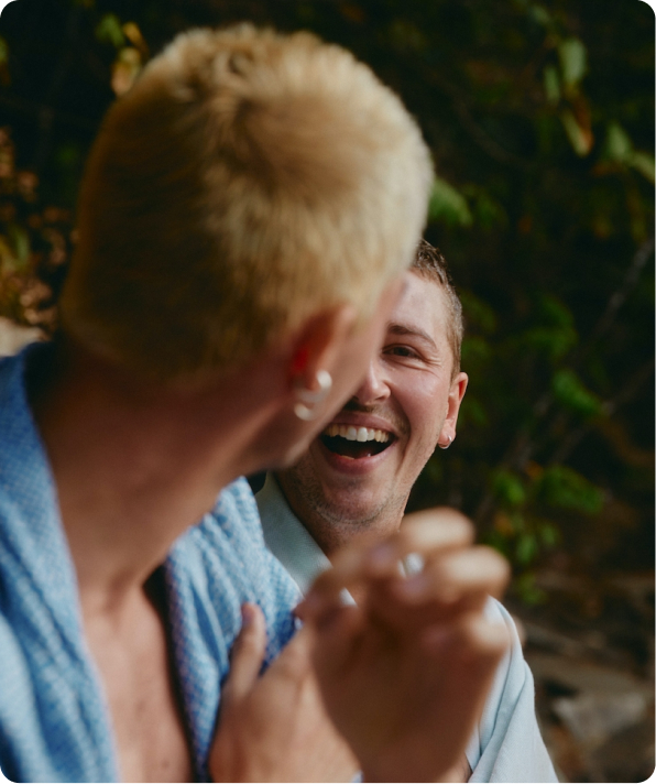 Two men laughing and talking outdoors with one man blurred in foreground.