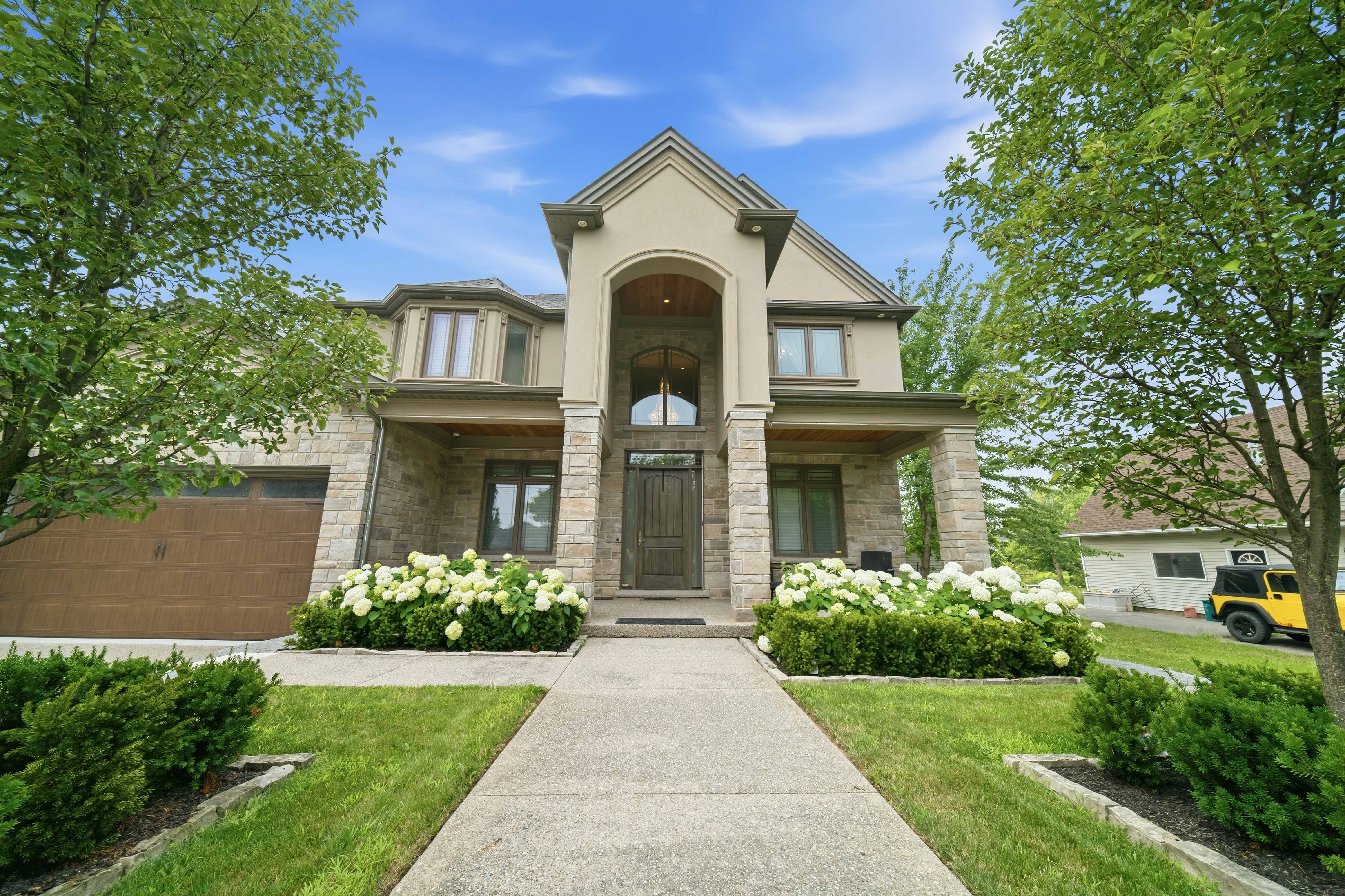 294 Tanbark Road, Niagara-on-the-Lake — front elevation of the stone and stucco estate with arched entry and hydrangea beds