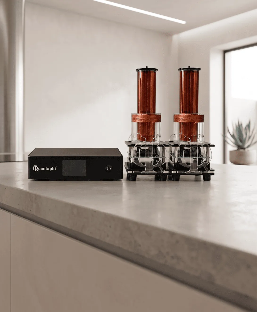 A Quantaphi device with a black control unit beside two copper Tesla coils in glass housings on a kitchen counter