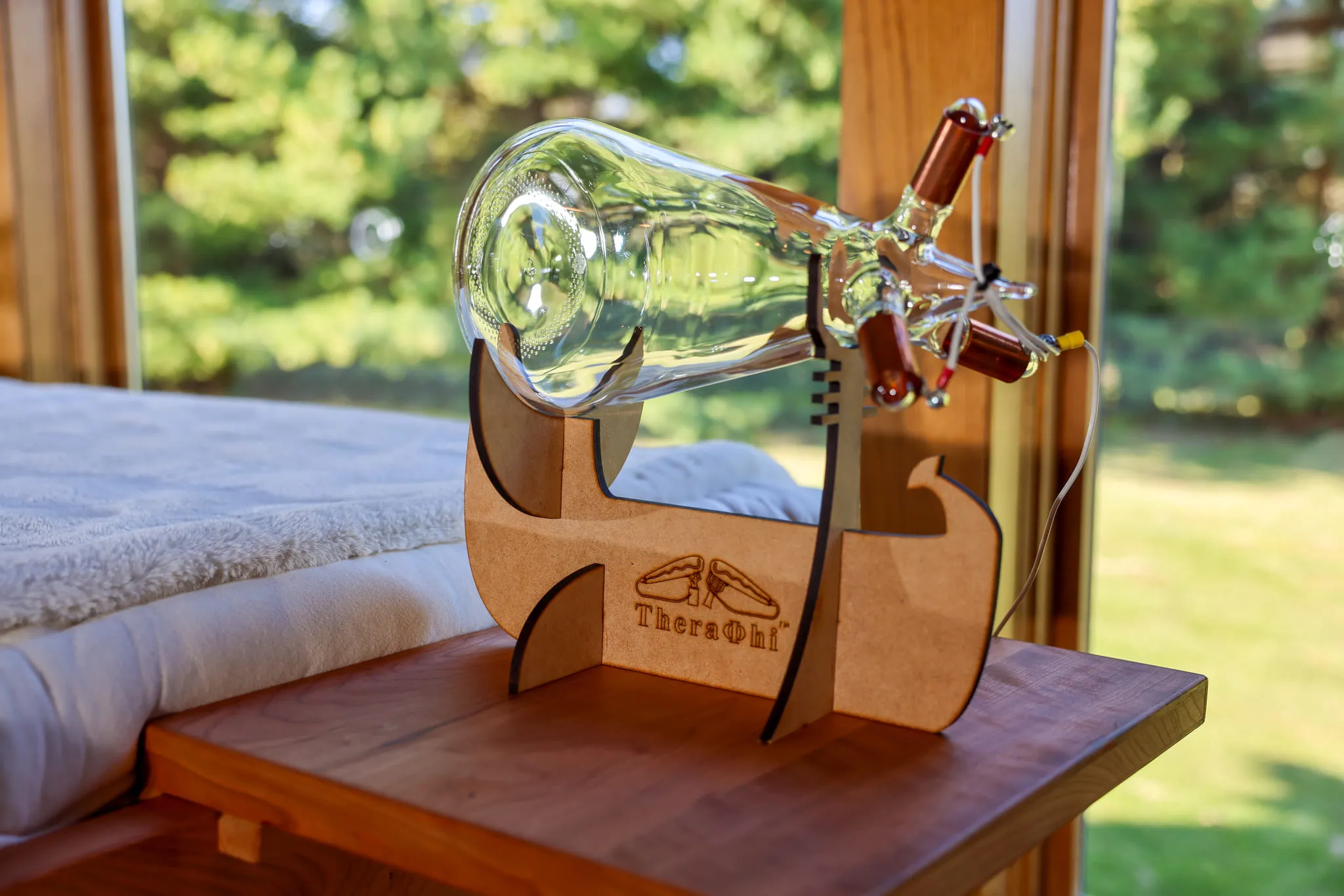 A Theraphi glass plasma tube on its wooden stand beside a window and massage table