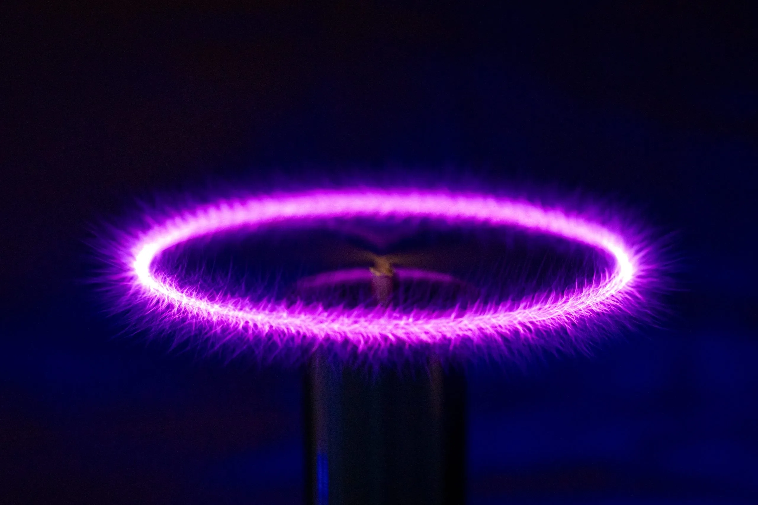 A bright purple corona discharge forming a ring of light above a Tesla coil