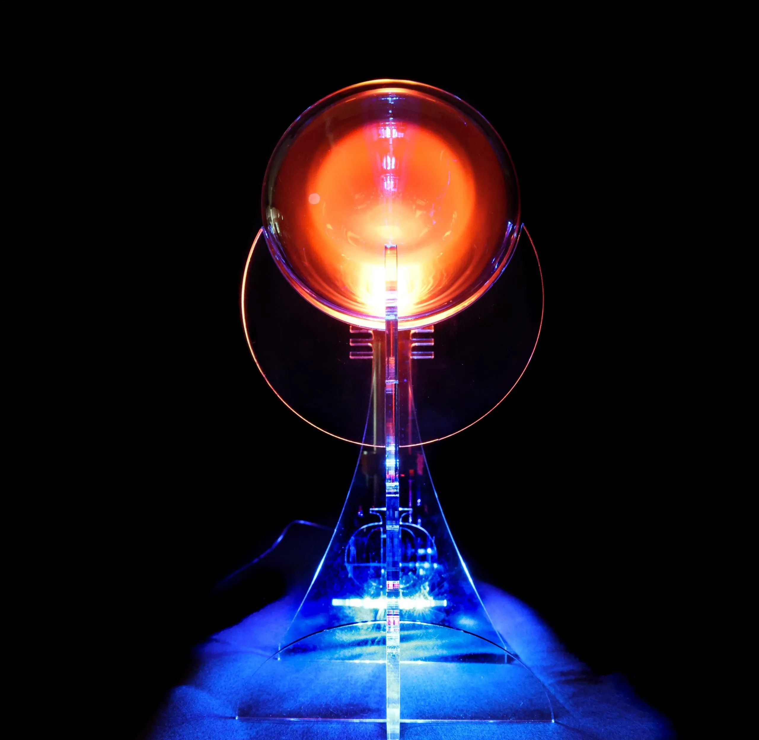 A glowing orange plasma orb on a clear acrylic stand lit from below with blue light