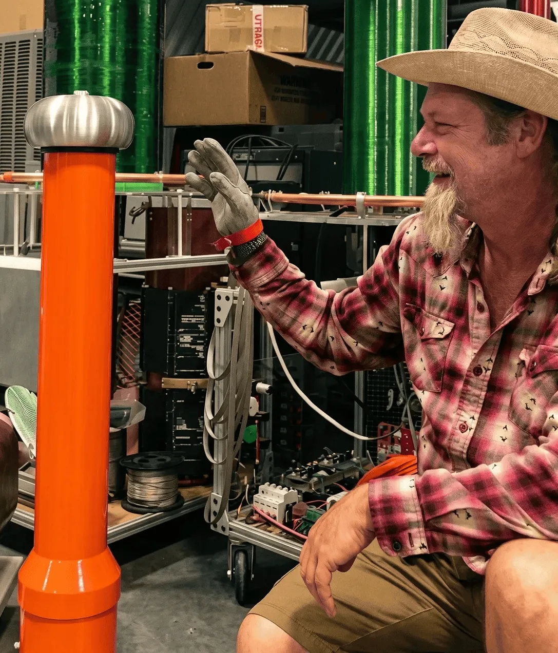 Paul Harris examining an orange plasma coil device in his workshop, surrounded by electronics and test equipment