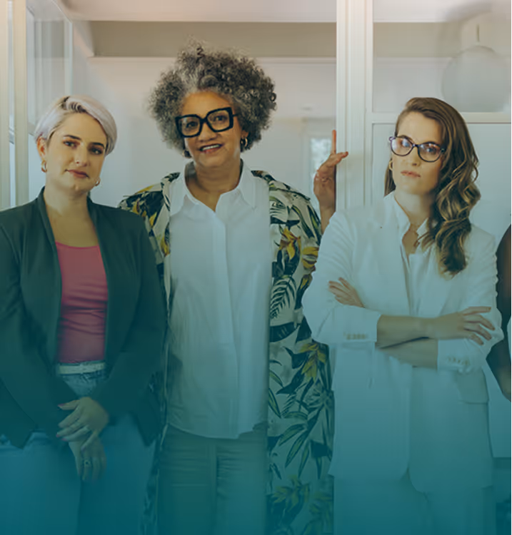 A diverse group of five professional women standing together confidently in a brightly lit office setting.