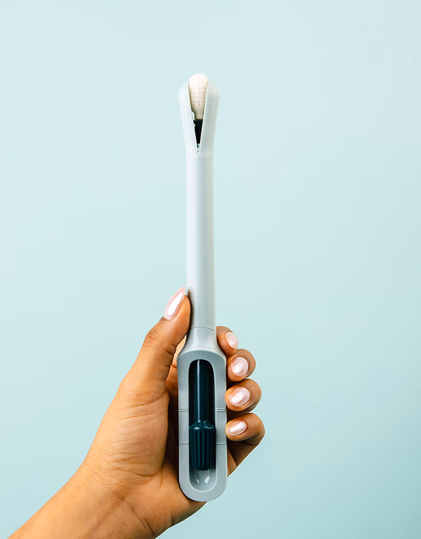 A close-up shot of a hand with manicured nails holding the Teal Wand cervical cancer screening device upright against a seamless light blue background, showcasing the device's soft collection tip and handle design.
