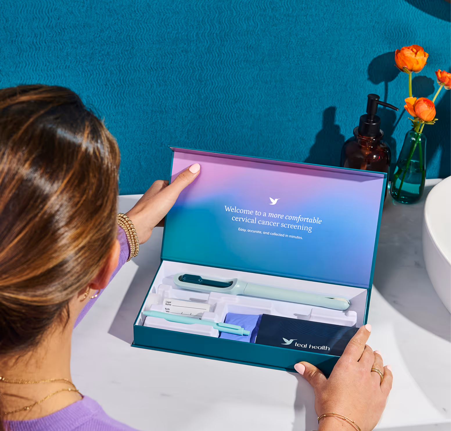 An overhead view of a woman opening a Teal Health cervical cancer screening kit on a white bathroom vanity. The inside lid reads "Welcome to a more comfortable cervical cancer screening" and neatly houses the Teal Wand, sample labels, and collection accessories.