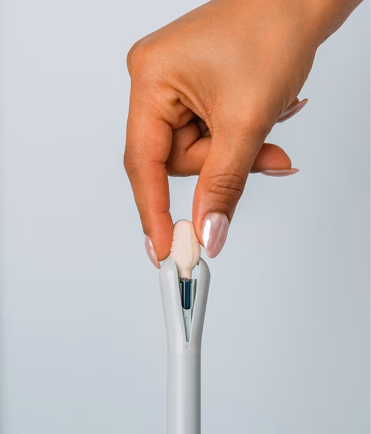 A close-up demonstration of a hand gently pinching the soft collection sponge tip of the Teal Wand device against a clean gray background, highlighting the comfortable design of the at-home cervical cancer screening device.