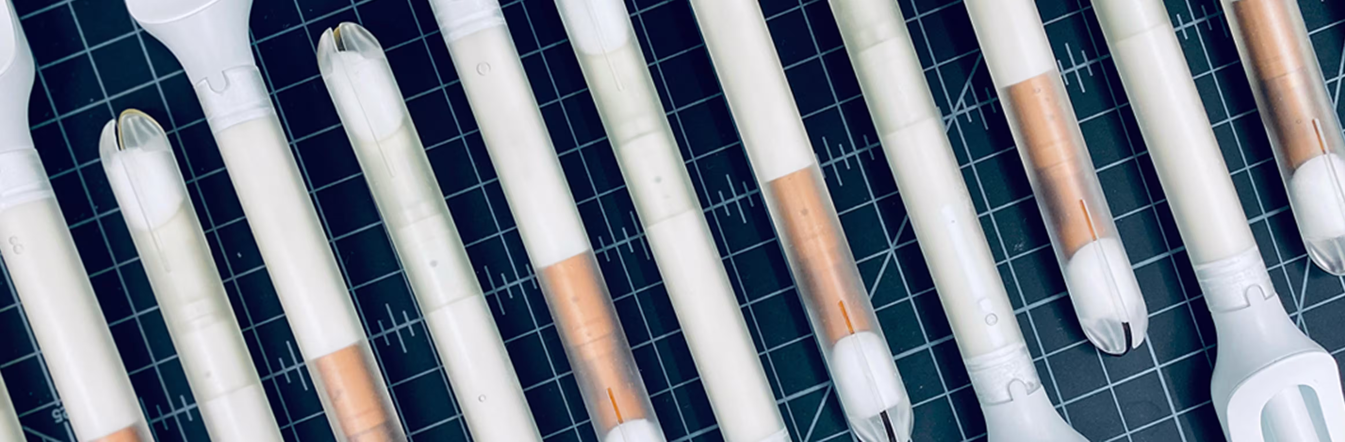 A top-down grid view of multiple white and clear medical device prototypes for the Teal Wand arranged diagonally on a black cutting mat with grid lines, showcasing the product engineering and design phase.
