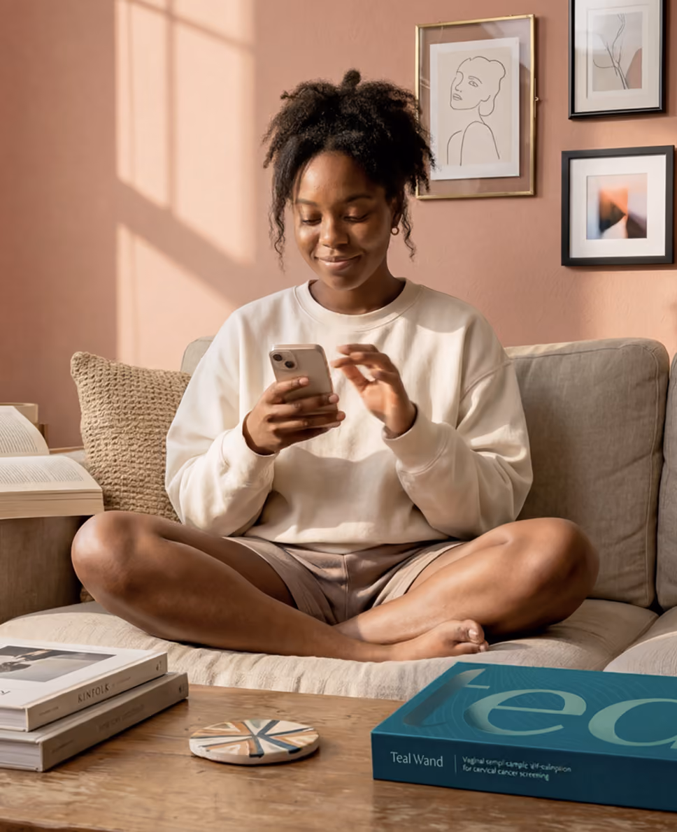 Young woman sitting cross-legged on a couch smiling at her phone, with a teal Teal Wand box on the table.