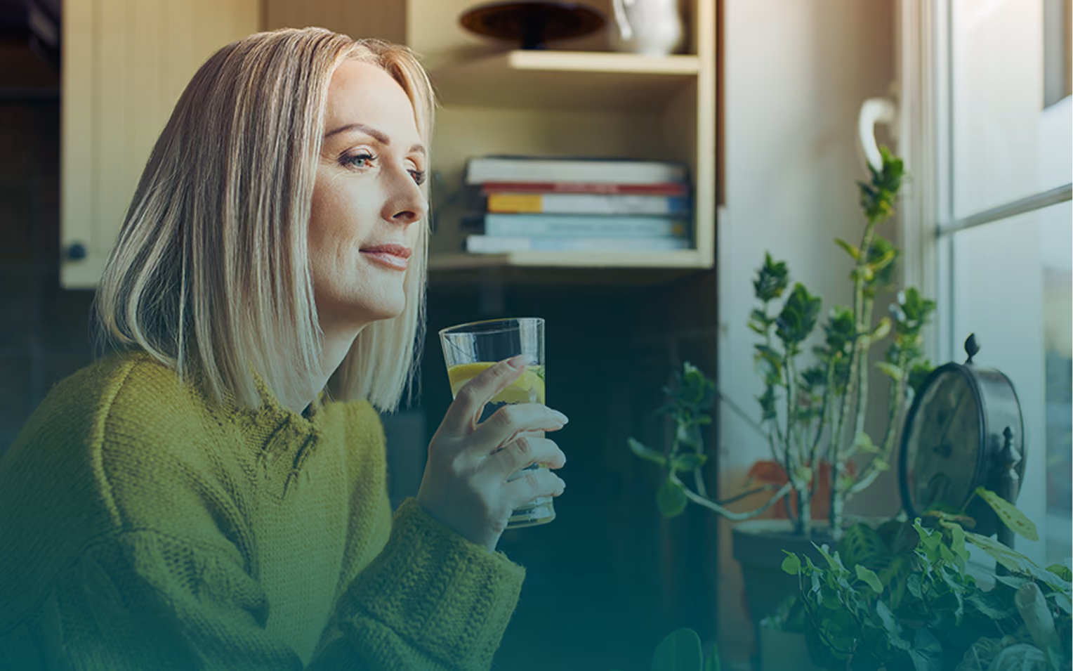 A woman looking out a window while holding a glass of water, surrounded by indoor house plants in a warm kitchen setting.