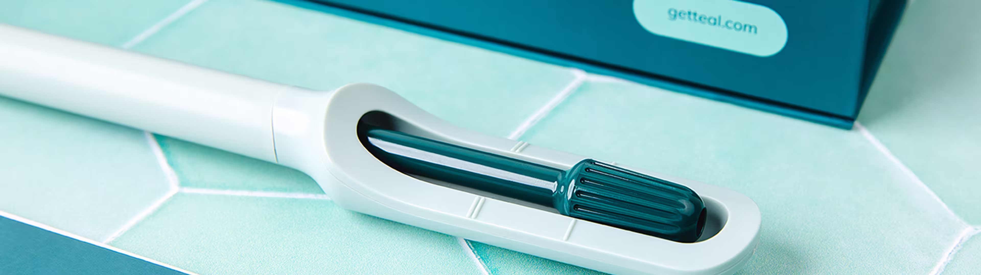 Close-up of the mint self-collection wand on a pale tiled surface; dark box behind reads getteal.com.
