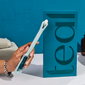 A hand holds up the light-teal colored Teal Wand self-collection device next to its vertical product packaging on a white marble bathroom vanity, showcasing its modern, user-friendly design.
