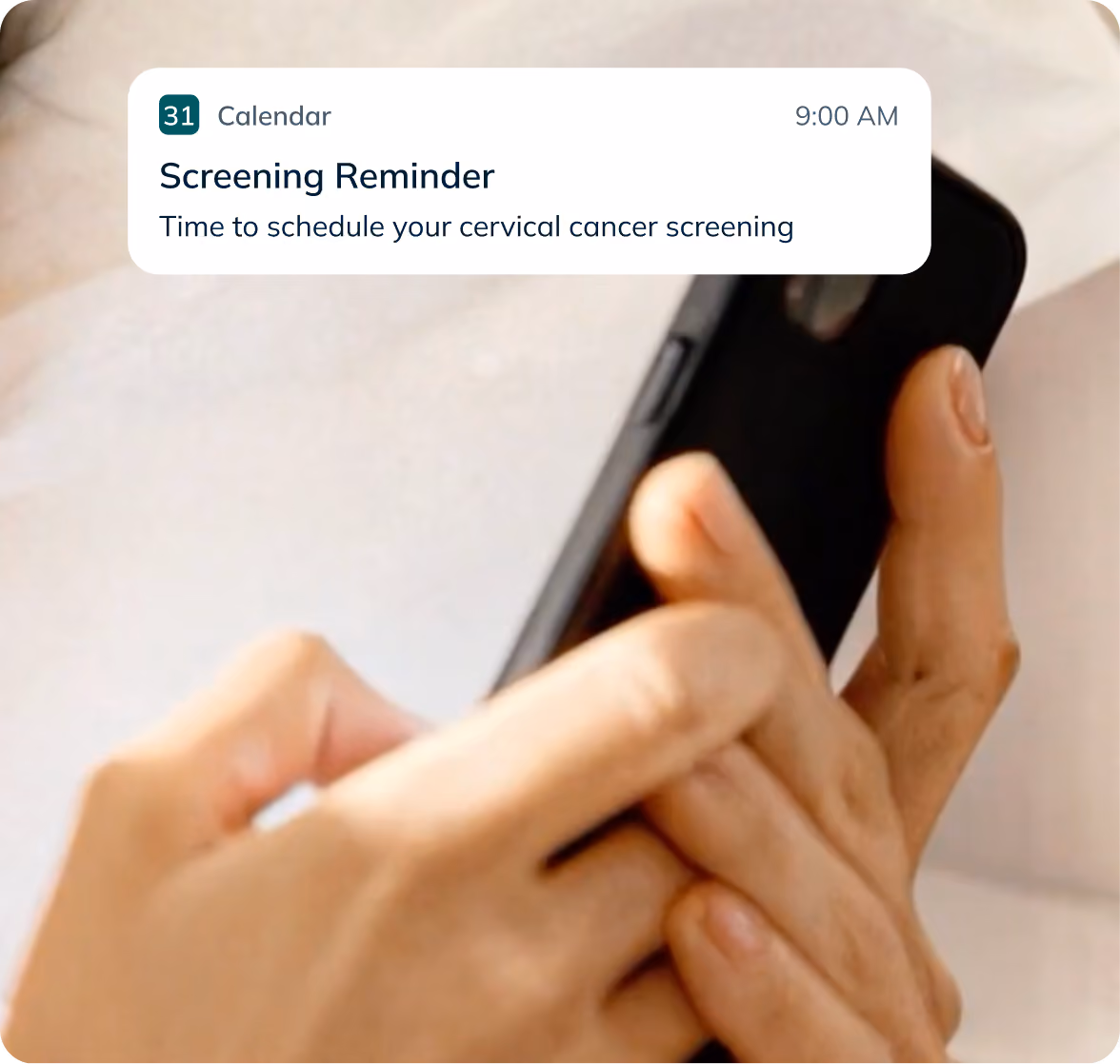 A close-up shot of a person's hands holding and typing on a black smartphone against soft white bed linens, highlighting easy mobile health notifications and screening reminders.