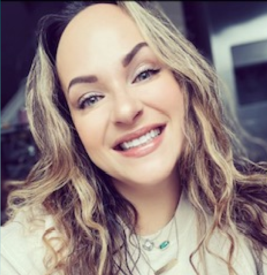 Smiling woman with wavy blonde hair and blue eyes in a close-up selfie.