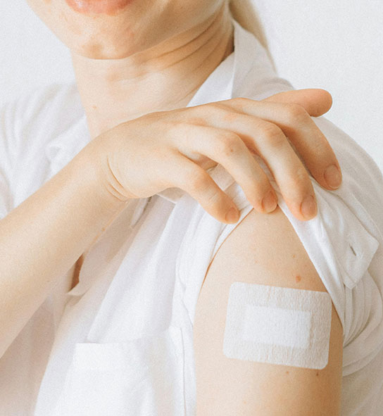 Close-up of a bare shoulder with a white adhesive bandage, shirt sleeve pulled up.