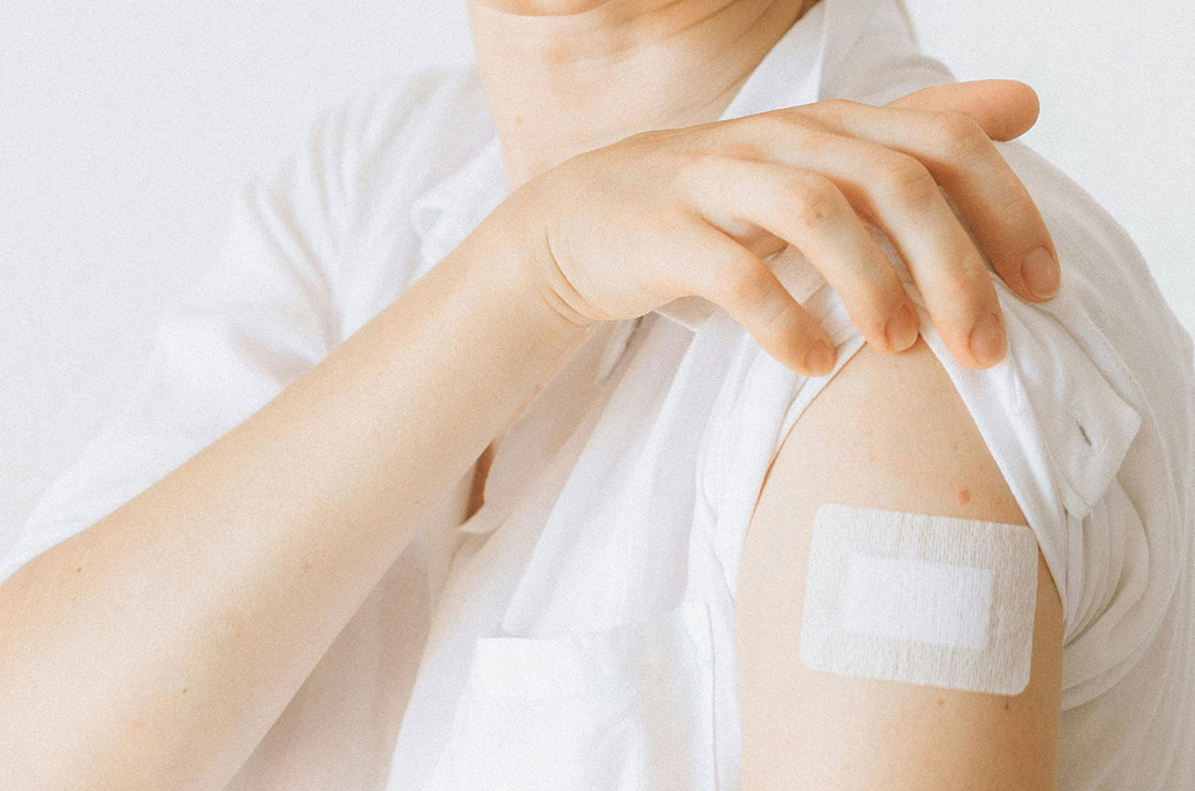 Close-up of a bare shoulder with a white adhesive bandage, shirt sleeve pulled up.