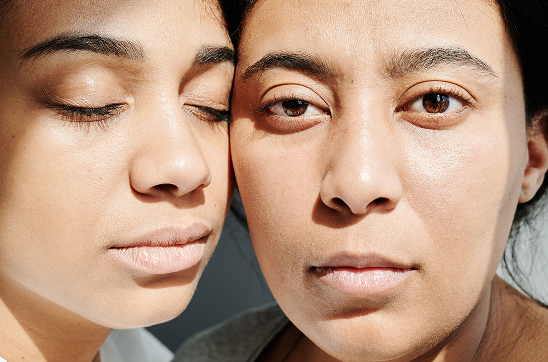 Close-up of two women's faces cheek to cheek, one with eyes closed, the other gazing forward.