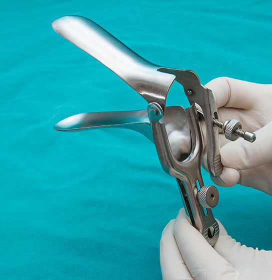 Gloved hands hold a stainless steel vaginal speculum over a teal cloth.
