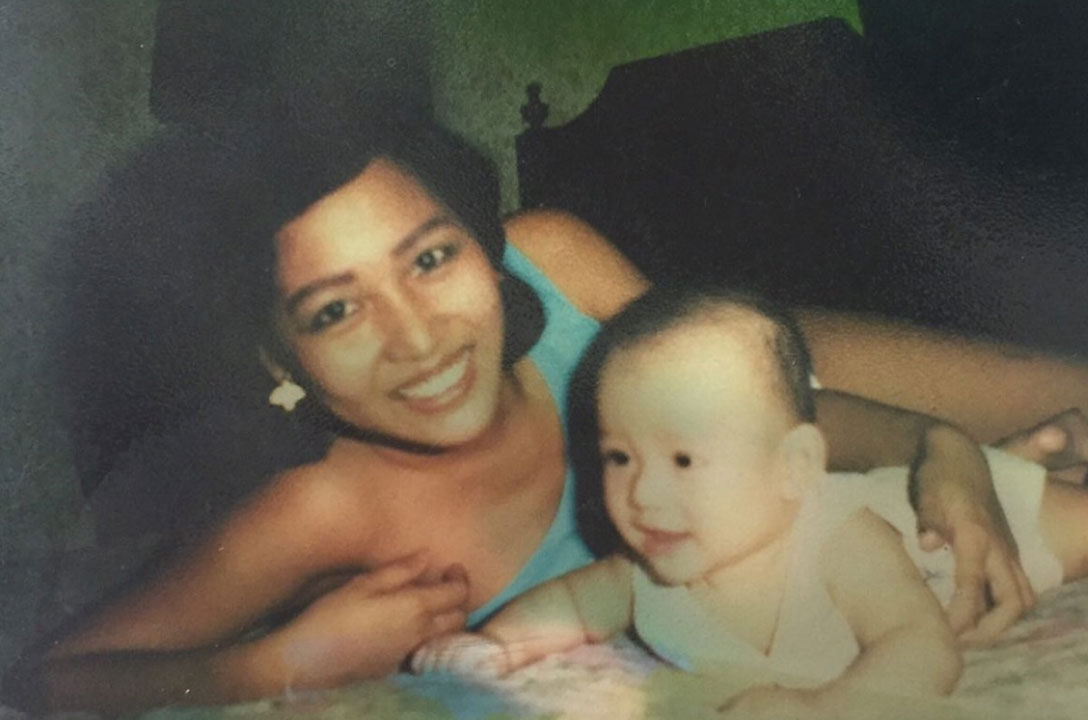 Vintage snapshot of a smiling woman lying on a bed beside a baby.