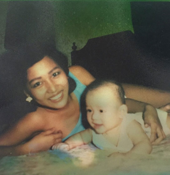 Vintage snapshot of a smiling woman lying on a bed beside a baby.