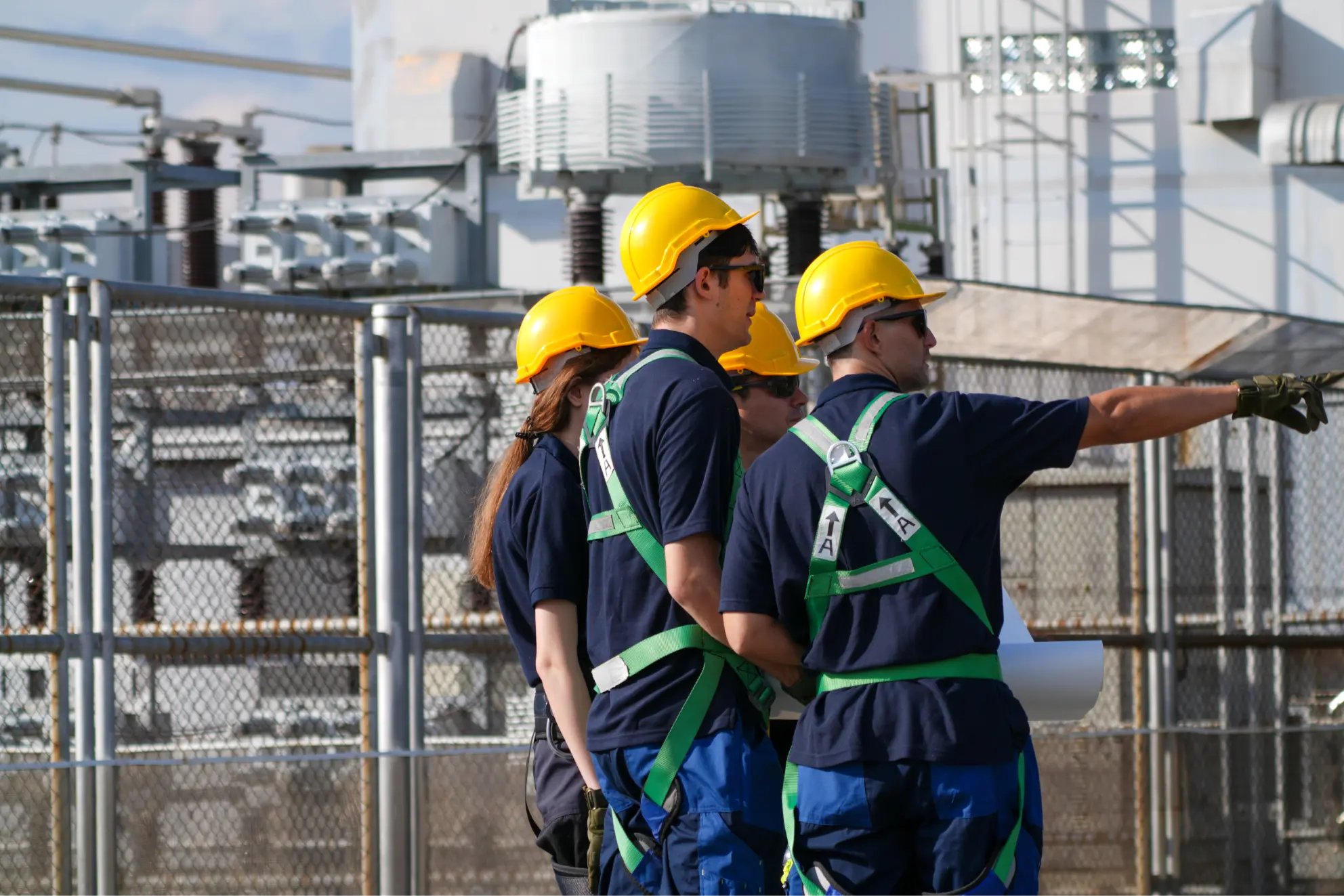 Field technicians in yellow hard hats and harnesses gathered outside an electrical facility.