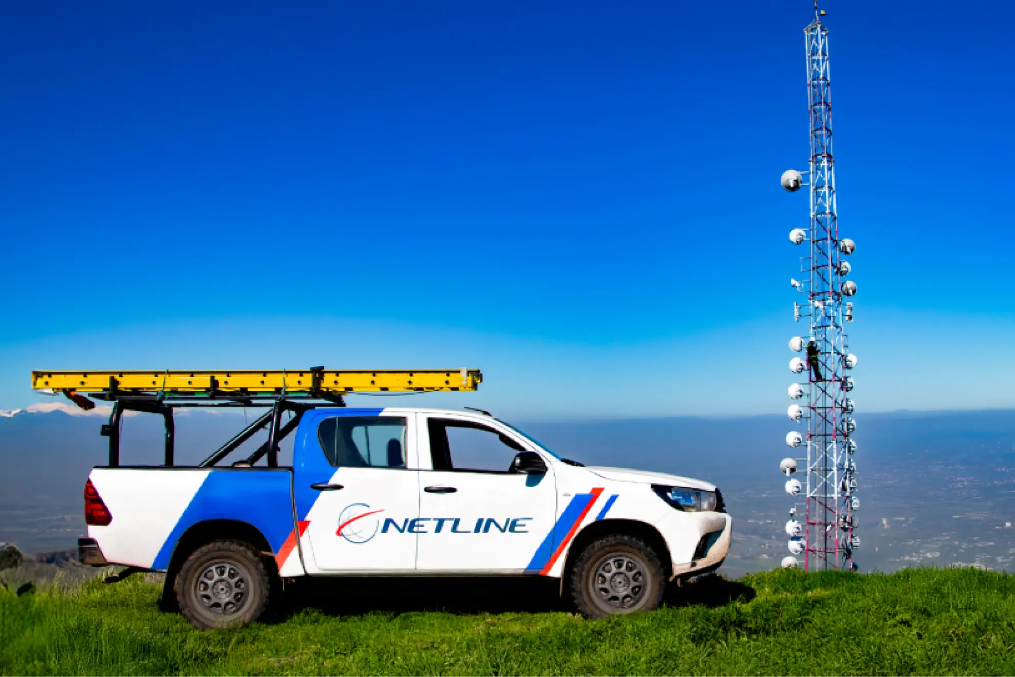 Netline pickup truck with ladder rack parked on a hilltop beside a telecom tower.