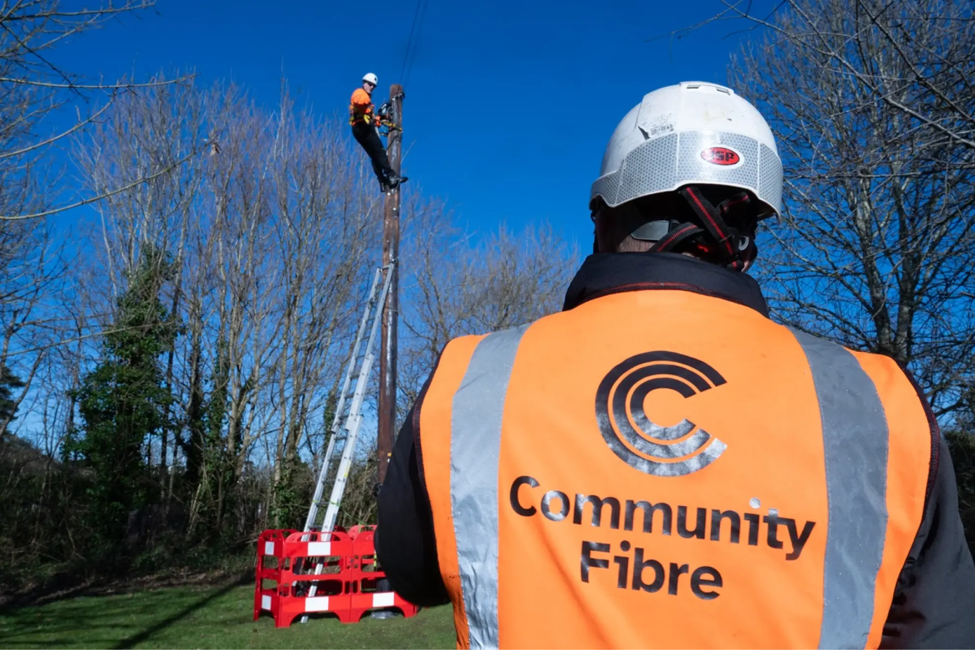 Community Fibre engineer watching a colleague climb a telegraph pole to install fibre.