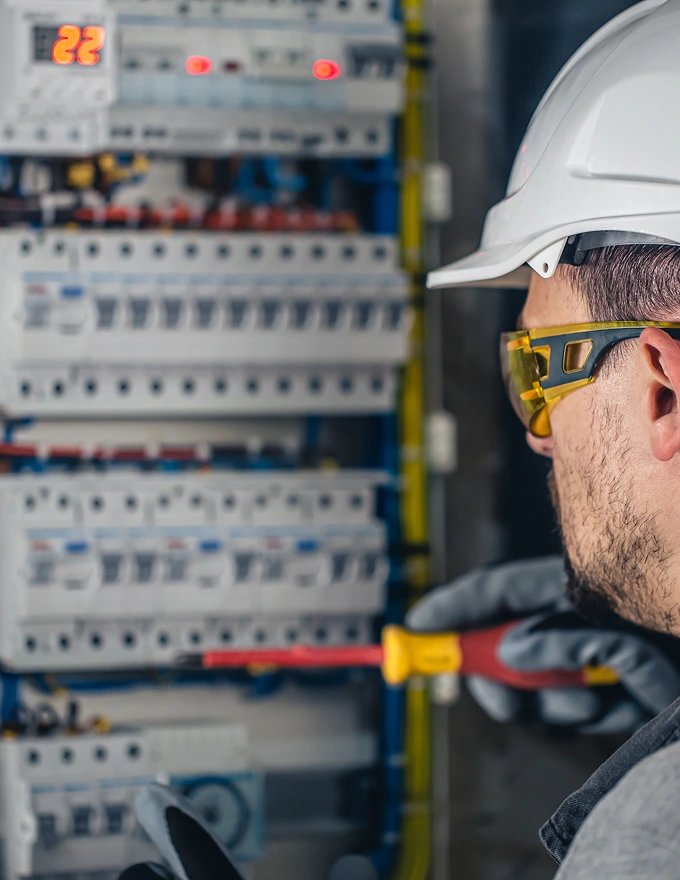 Electric utility technician in a hard hat and safety glasses working on a circuit breaker panel.