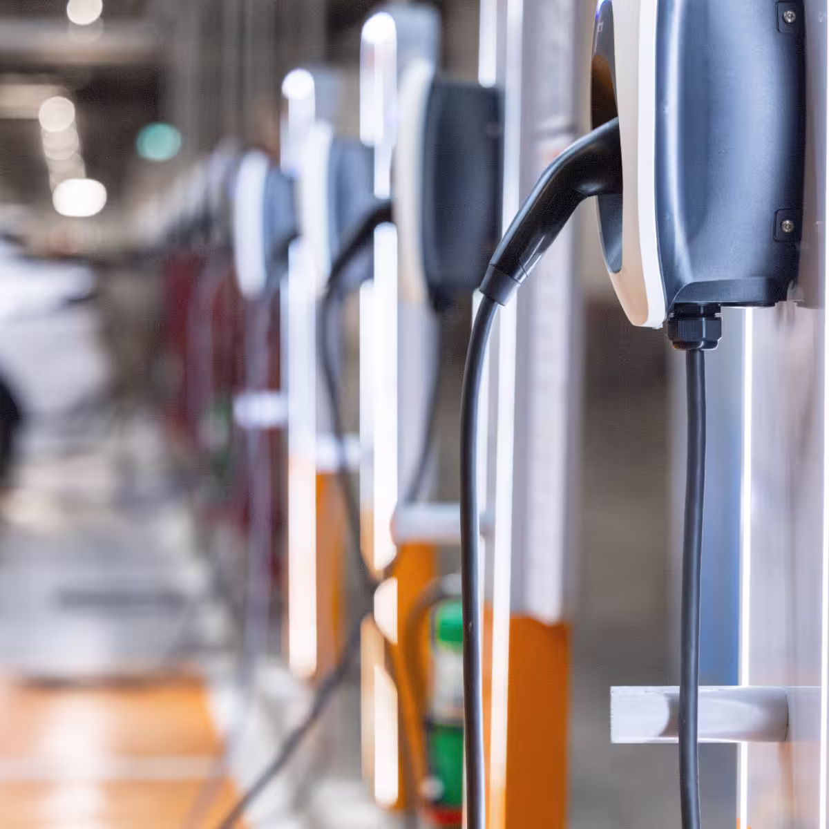 Row of wall-mounted EV chargers with cables in a parking garage.