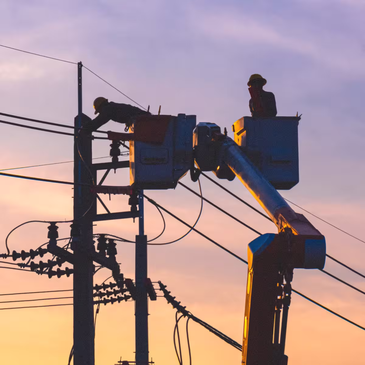 Line workers in bucket trucks repairing overhead power lines at sunset.