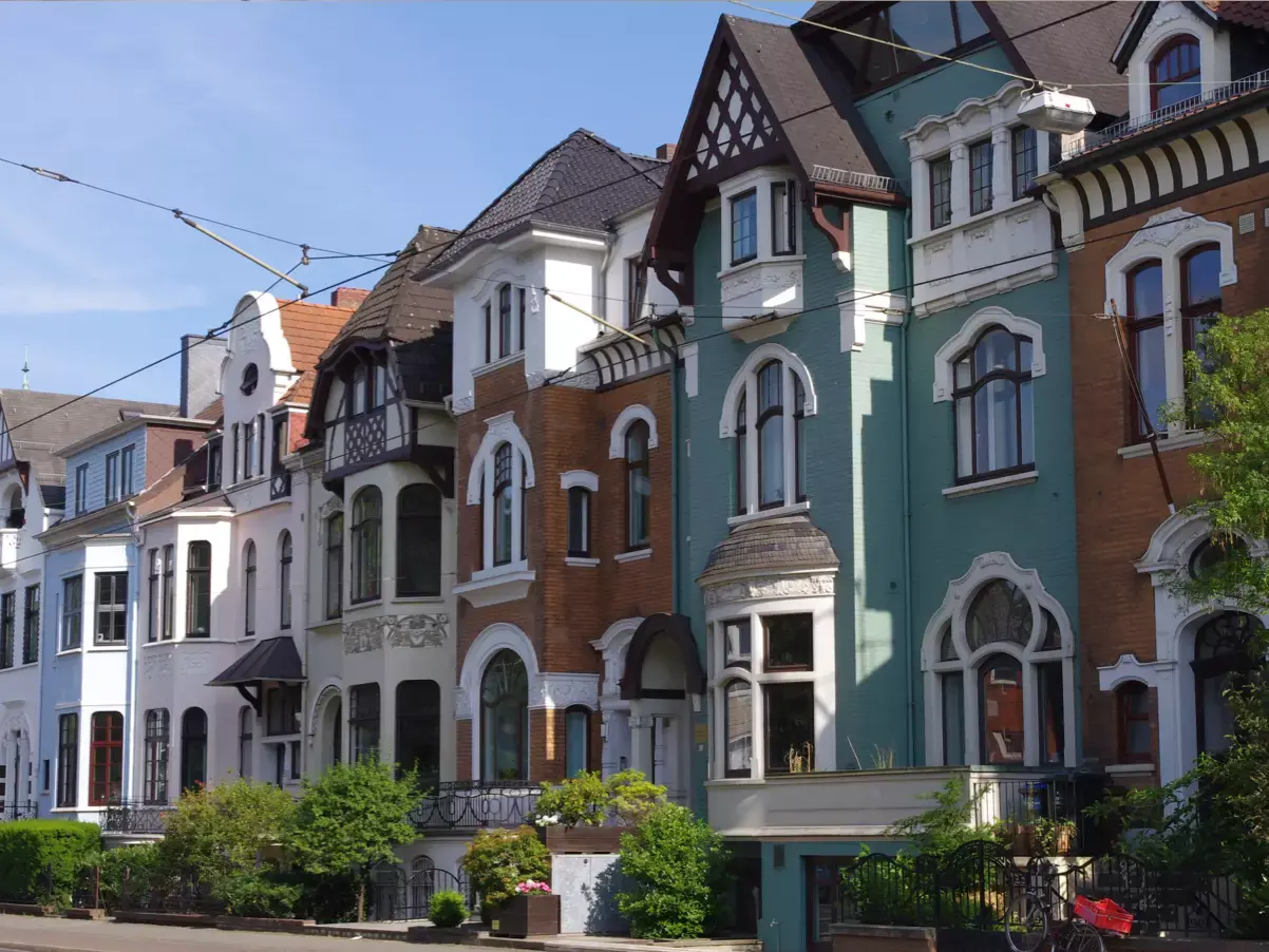 Mehrere historische Stadthäuser mit Ziegel- und Putzfassaden an einer Straße unter blauem Himmel.