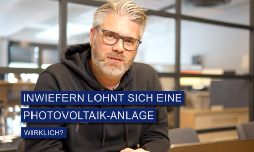 Mann mit Brille und grauen Haaren spricht vor modernem Bürohintergrund über Photovoltaik-Anlage.
