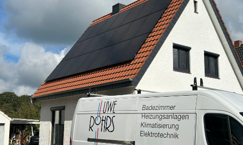 Weißes Haus mit schwarzen Solarmodulen auf dem Dach und einem Handwerker-Van davor.