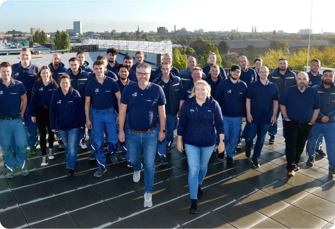 Gruppenfoto von Mitarbeitern in blauer Arbeitskleidung, die auf einem Dach bei Tageslicht stehen.