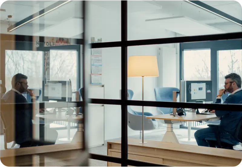 Zwei Männer in Anzügen arbeiten konzentriert an Computern in einem modernen Büro mit Glaswänden.