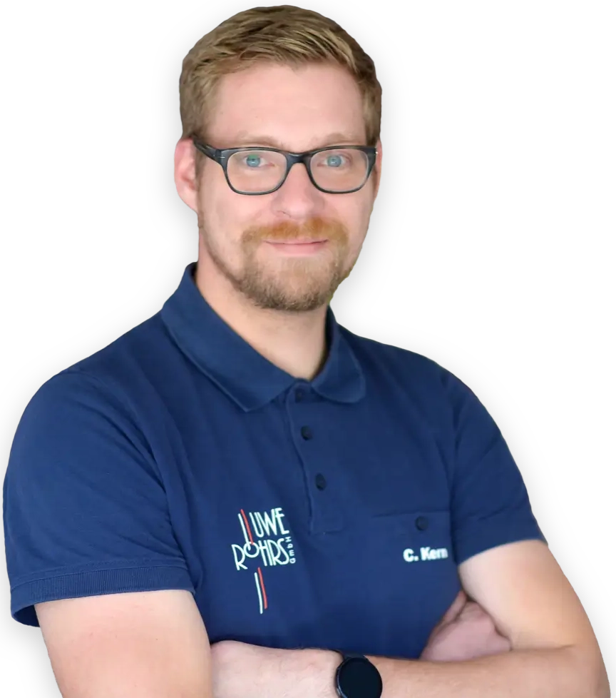 Mann mit Brille in blauem Polohemd mit verschränkten Armen vor schwarzem Hintergrund.
