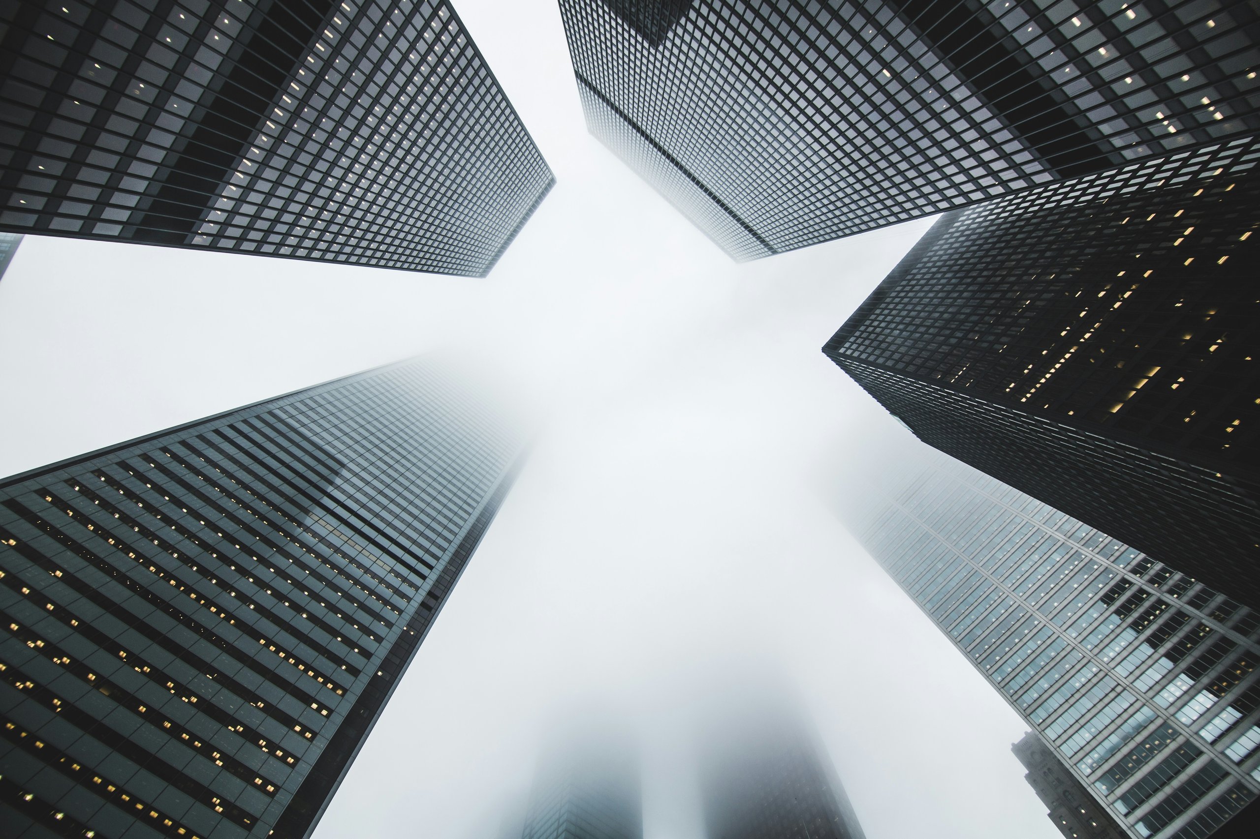 Low-angle view of multiple tall skyscrapers with fog obscuring their tops.