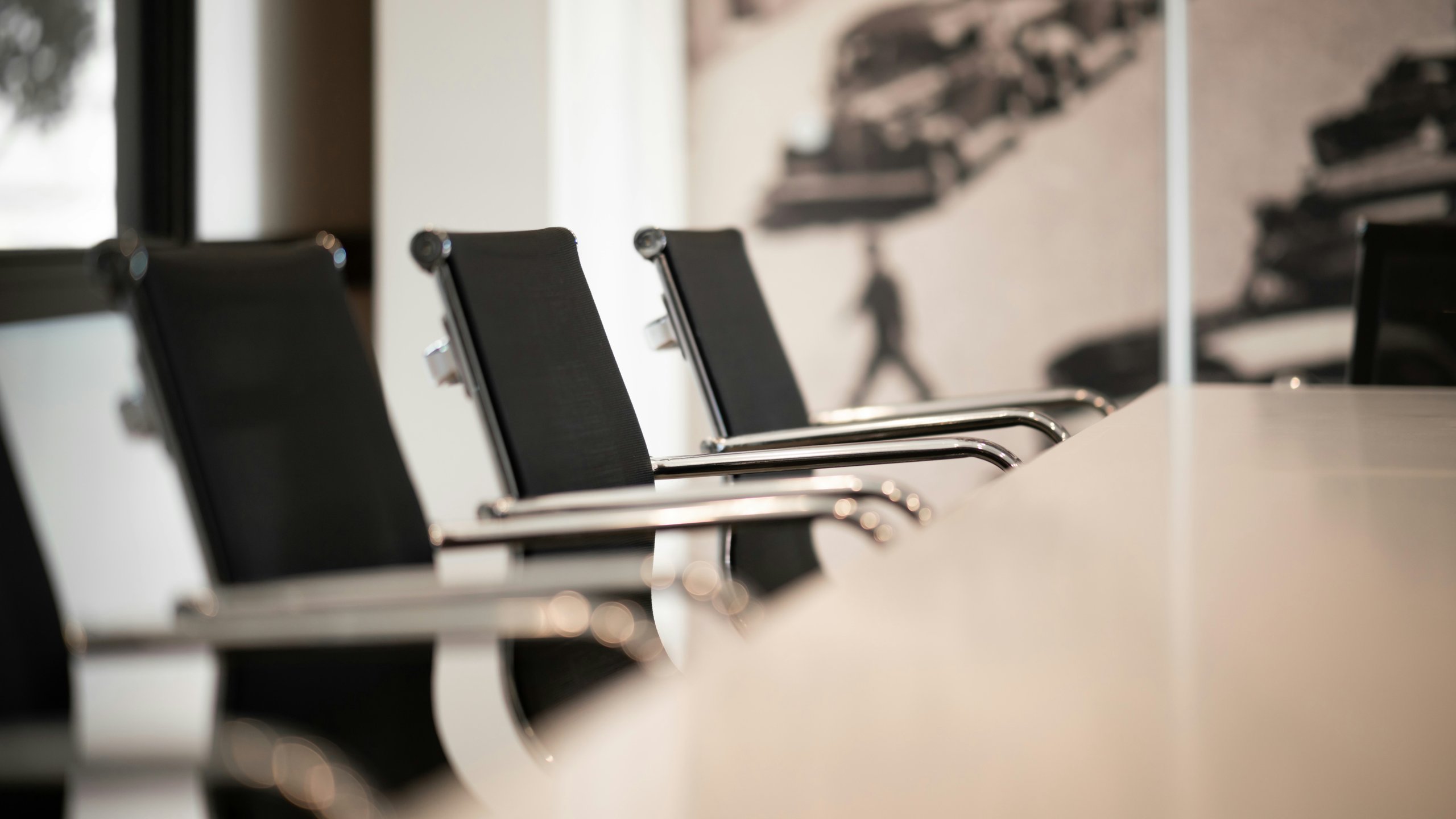 Three black office chairs with metal armrests along a white conference table.