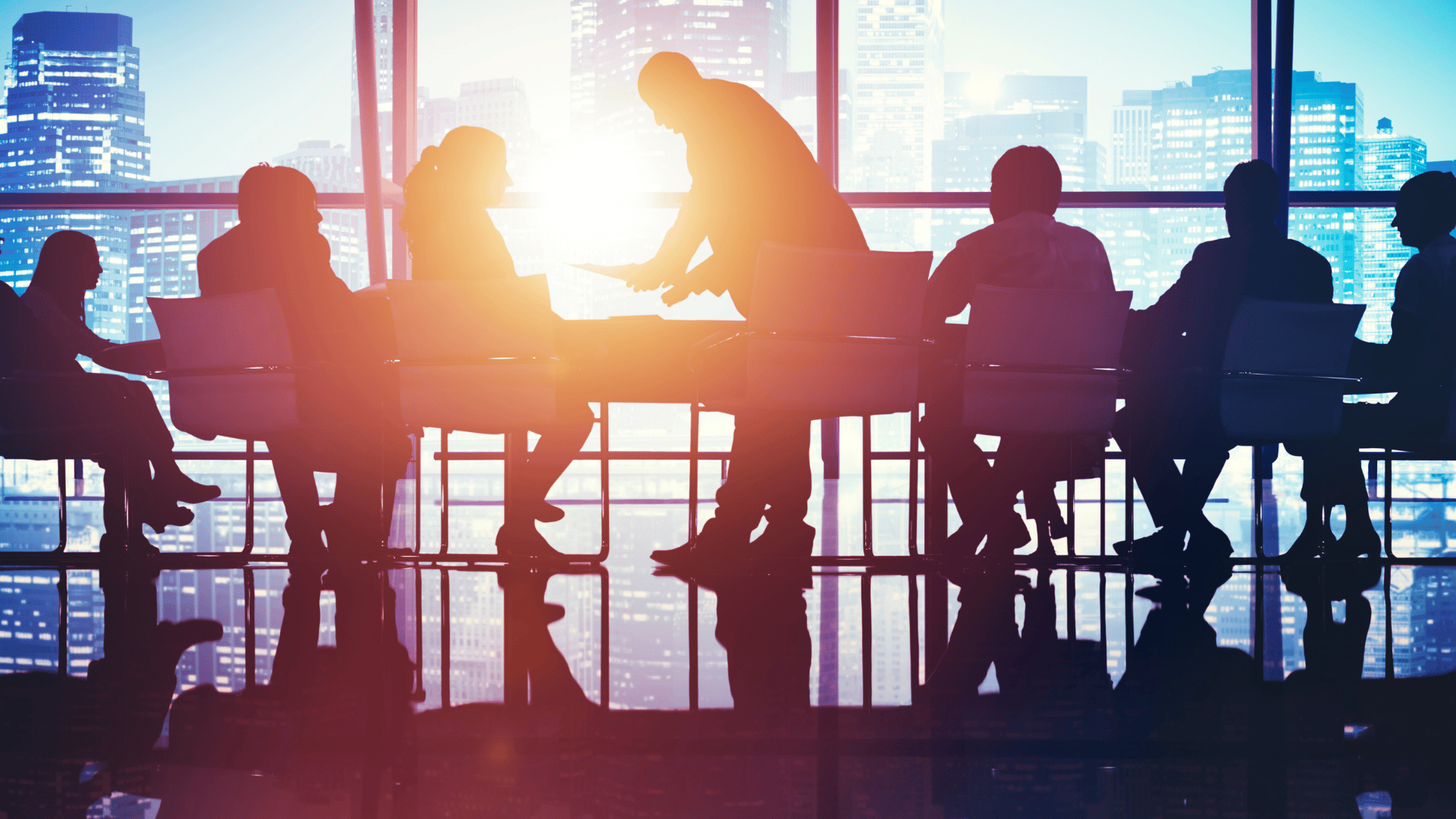 Silhouettes of people in a business meeting with city skyline and sunlight in the background.
