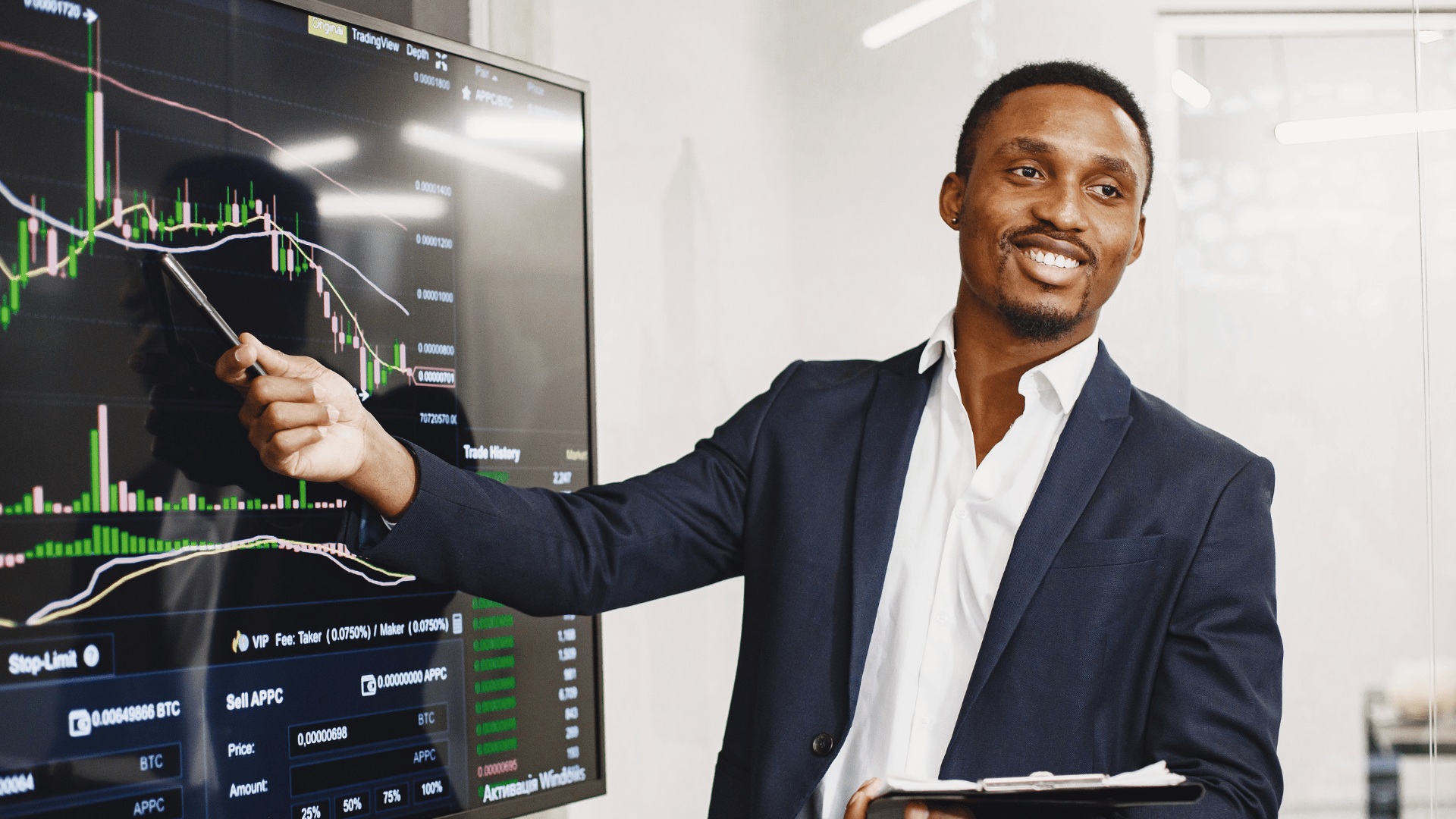 Man in suit pointing with pen at financial chart with green and red candlesticks on a display screen.