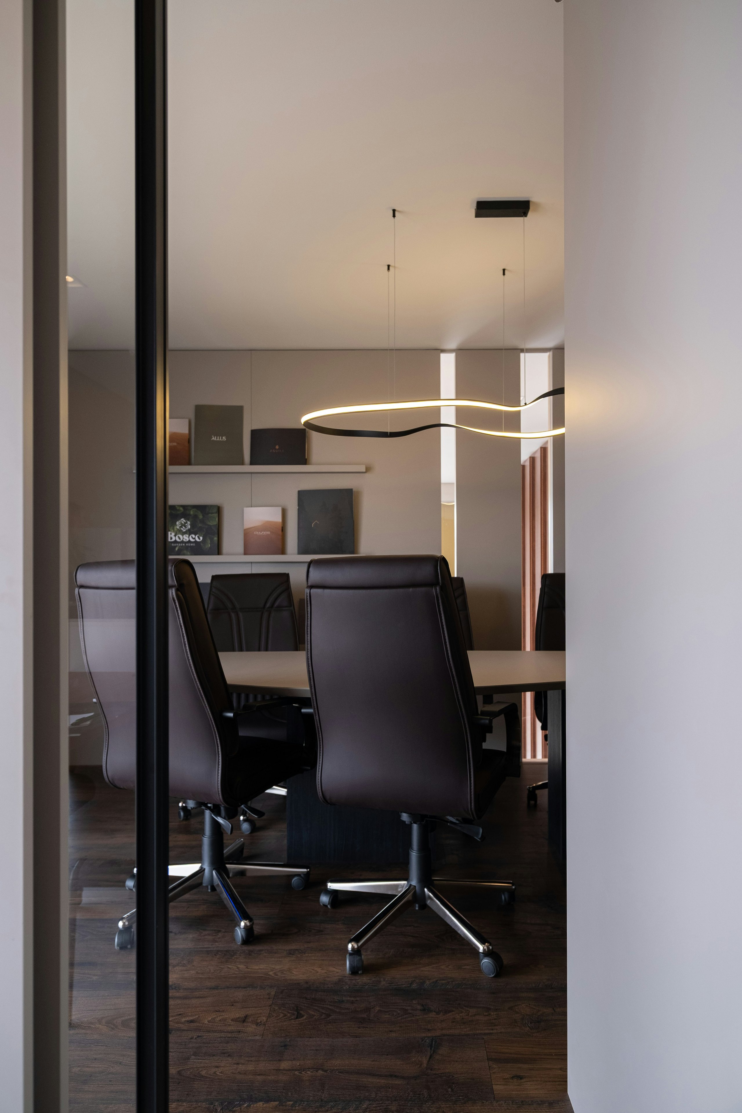 Modern conference room with black leather chairs, wooden floor, table, and wavy ceiling light.