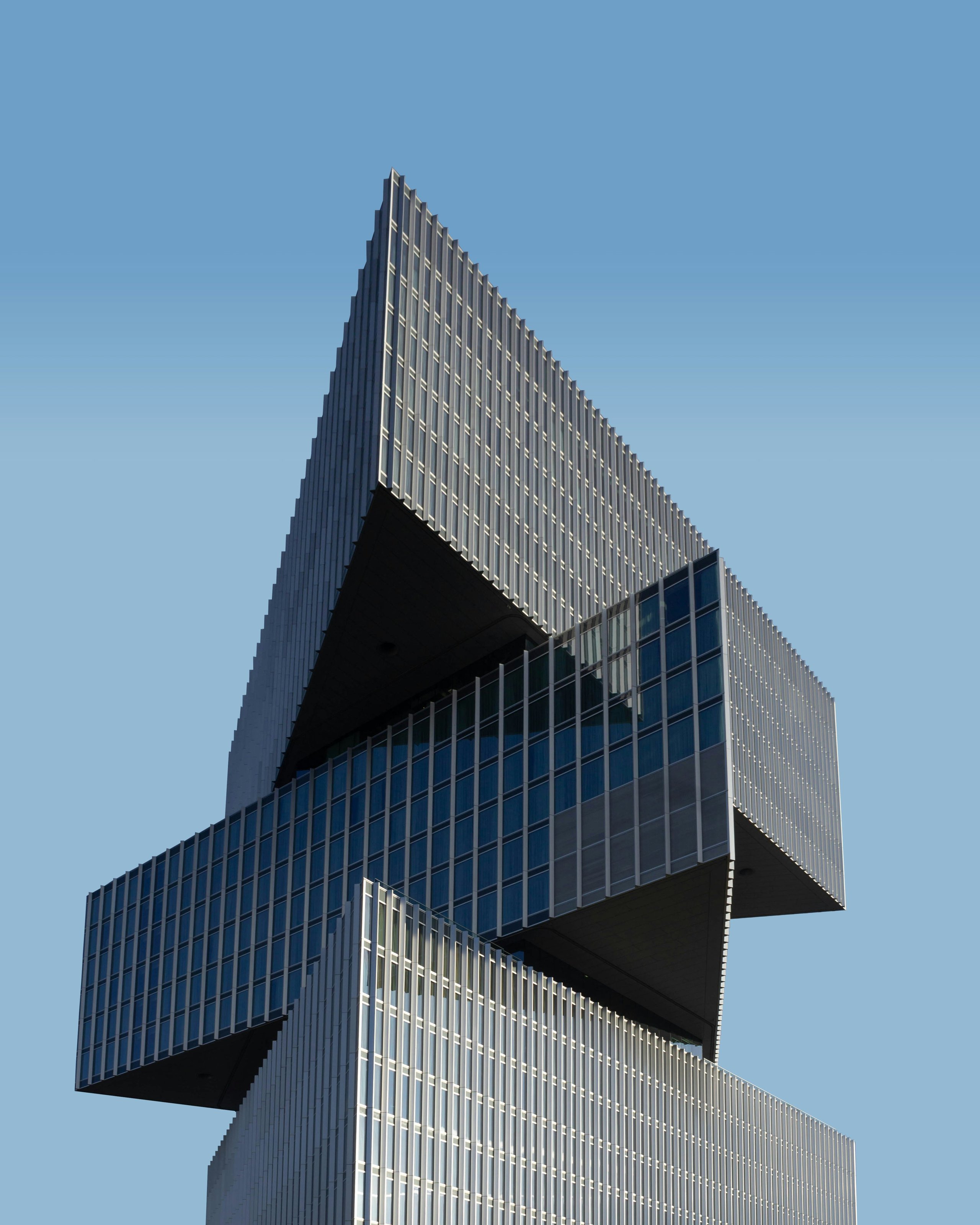 Modern high-rise building with stacked sections and blue reflective glass against clear sky.