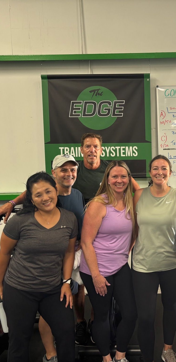Group of nine smiling members posing together inside The EDGE gym in Glenview